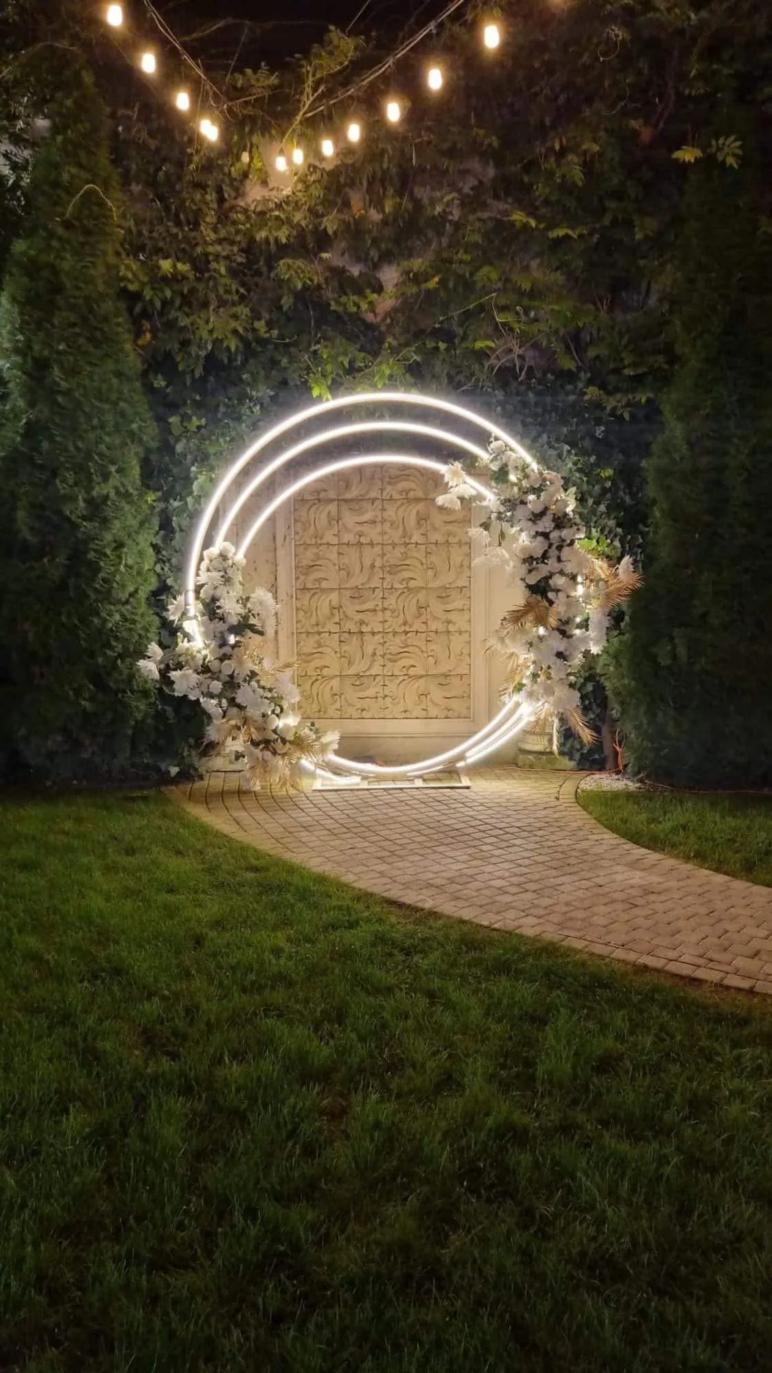 Arcadă circulară cu neon și flori albe, decor ceremonie de noapte în grădină